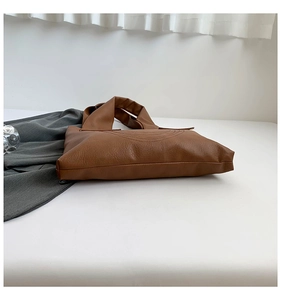 Close-up of brown PU leather tote bag with curved stitching and wide shoulder strap