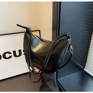 Detail of glossy black hobo bag with unique knotted strap and gold metal zipper