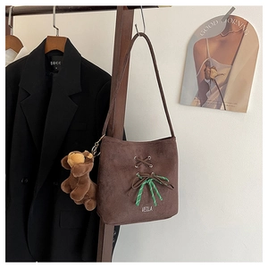 Detail of dark brown suede bucket bag featuring lace-up design and a plush dog charm
