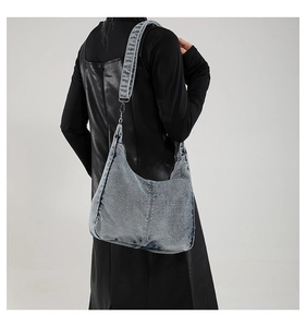 Detail of light blue denim hobo bag with wide shoulder strap and silver metal hooks