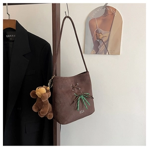 Detail of a brown suede tote bag with green bow decoration and bear charm
