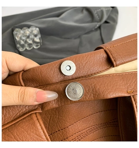 Detail of silver magnetic closure on brown lychee texture tote bag with fine engraving