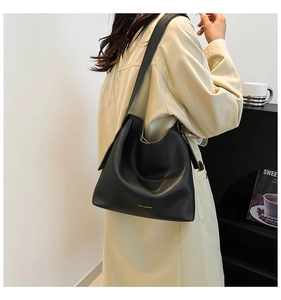 Detailed macro view of black matte leather hobo bag with gold logo on beige trench coat
