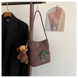 Detail view of brown suede bucket bag with striped ribbon and plush bear charm
