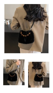 Detail of plush black faux fur crossbody bag with amber bead and leather strap