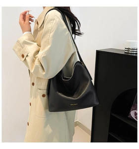 Detail of black lychee grain leather hobo bag with gold logo on khaki trench coat
