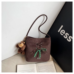 Detail view of brown suede bucket bag featuring striped bow and cute plush bear charm