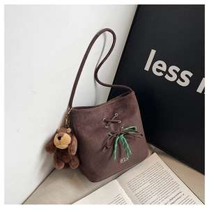 Detail of dark brown suede bucket bag featuring embroidered logo and a cute bear charm