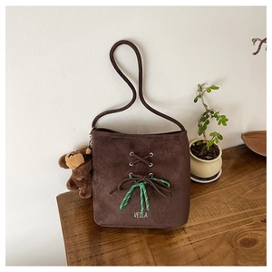 Detail of coffee brown suede bucket bag with cross straps and plush monkey charm