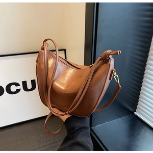 Close-up of brown crescent hobo bag with knotted shoulder strap and golden metal hooks
