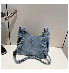 Detailed macro view of the blue denim half-moon shoulder bag with white stitching