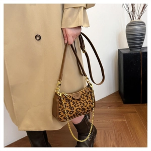 Close-up of leopard print baguette bag with gold chain and leather trim on a model