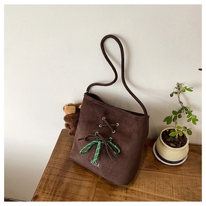Detailed close-up of dark brown suede bucket bag with knotted bow and brand logo