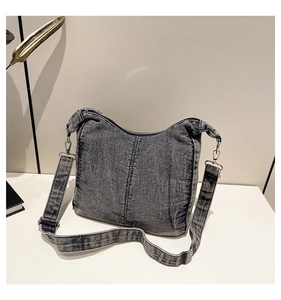 Detail of dark grey washed denim shoulder bag with silver hardware and adjustable strap