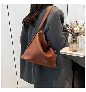 Close-up of brown leather bucket bag showing soft texture and gold logo on the model