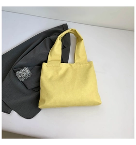 Close-up of bright yellow shoulder bag with crinkled leather texture on grey suit