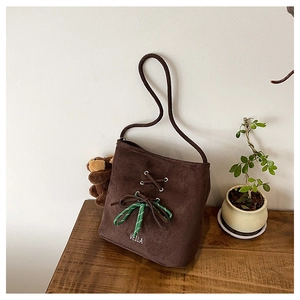 Close-up of brown suede bucket bag with decorative lace-up bow and logo detail