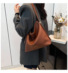Detail of a deep brown faux leather tote bag with gold logo and textured finish