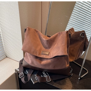 Detail of a brown suede tote bag with leather base and adjustable strap against a mirror