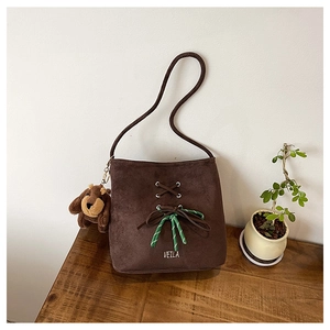 Detail view of suede bucket bag featuring lace-up metal eyelets and a cute bear charm