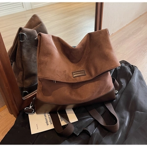 Detail of a large brown suede backpack with leather base and metallic buckle accents