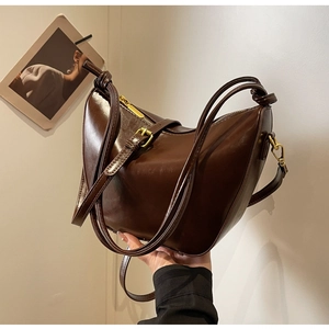 Detail of dark brown oil-wax leather shoulder bag with vintage gold zipper and strap knot