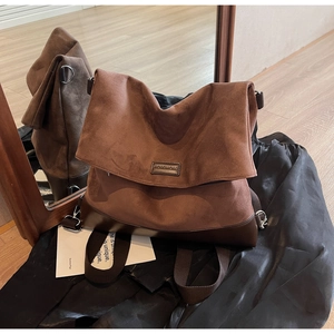 Detailed close-up of a vintage brown suede tote bag with metal branding and wide strap