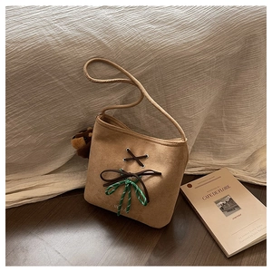 Close-up of brown suede shoulder bag with ribbon bow and plush bear charm detail