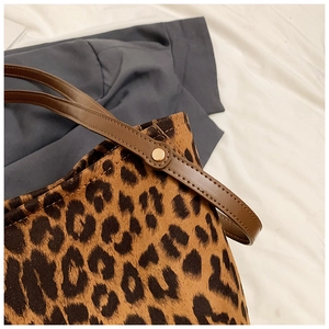 Detailed macro view of leopard print bucket bag with brown leather strap and gold rivet