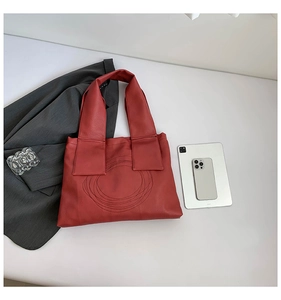 Flat lay of red leather tote bag with circular stitching and office accessories
