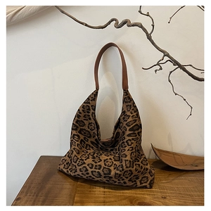 Detail of leopard print tote bag featuring brown leather straps on a wooden surface