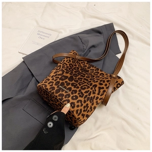 Detail view of leopard print bucket bag with brown leather straps on white fabric