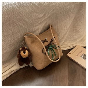 Detail of suede bucket bag with decorative bow tie and cute plush dog pendant