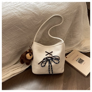 Detail of cream suede bucket bag featuring brown crisscross lacing and a blue bow charm
