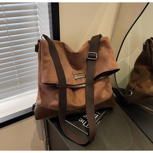 Detail of dark brown faux suede tote bag with wide canvas strap and metal logo
