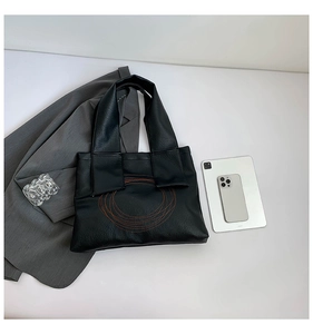 Close-up of black PU leather tote bag with brown circular embroidery and casual accessories