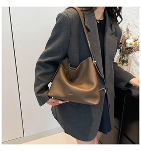 Detailed close-up of brown leather tote bag with gold logo and adjustable shoulder strap