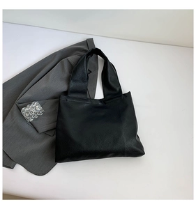Minimalist black leather tote bag shown with a gray blazer on a clean white background