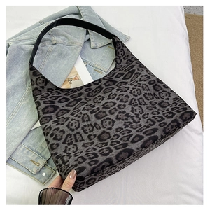 Detailed view of dark leopard print tote bag with black leather shoulder strap on white bed