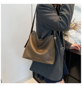 Detailed view of brown leather bucket bag with gold logo on a grey blazer model
