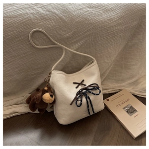 Detail of beige suede bucket bag featuring striped rope ties and a plush dog pendant