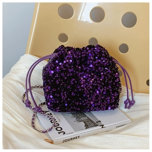 Dettaglio borsa a secchiello con paillettes viola e tracolla a catena su tavolo bianco
