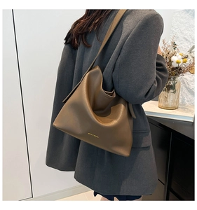 Detail view of large dark brown pebbled leather tote bag worn by a model in interior