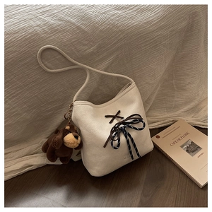 Close-up of beige canvas bucket bag with brown leather cord and plush puppy charm