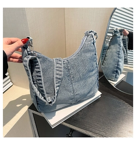 Close-up of light blue denim crescent bag showing washed texture and adjustable strap