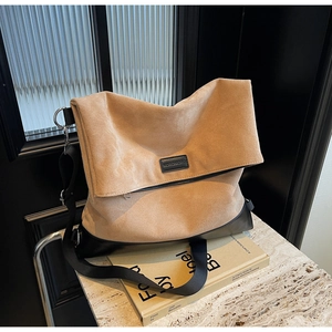 Detail of camel suede tote bag with black leather base and branded metal plate
