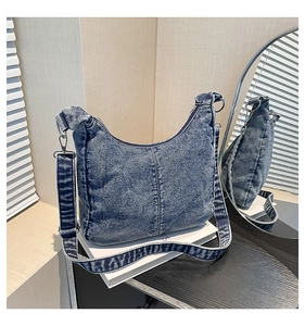 Detail of blue acid wash denim crescent bag with adjustable strap and silver hardware