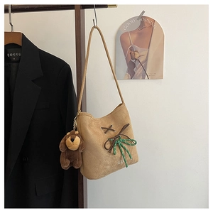 Detail of suede bucket bag featuring a brown bow, green rope, and plush puppy charm