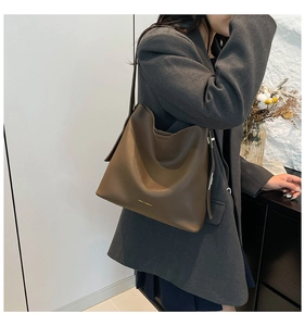 Brown leather tote bag with gold logo shown on shoulder with a grey blazer