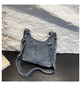Detailed view of dark blue washed denim shoulder bag with silver metal buckles